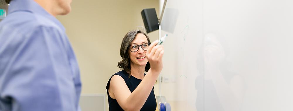woman talking to a colleague while writing on a whiteboard