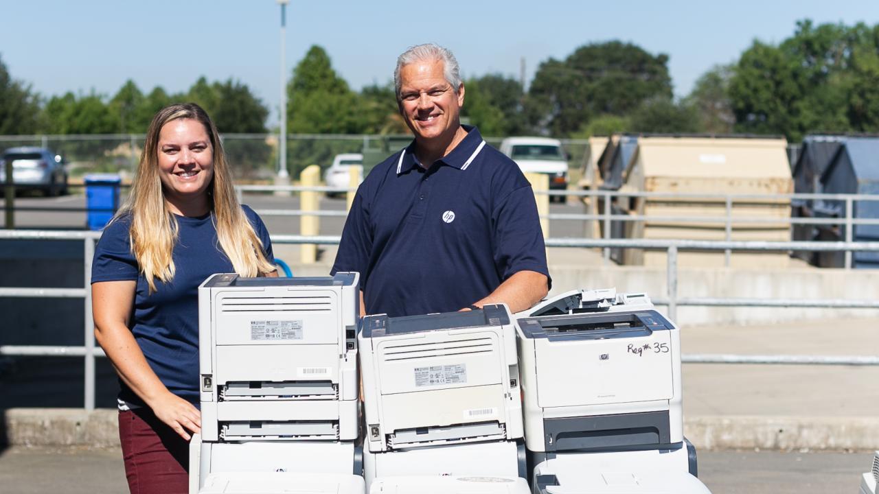 two uc davis employees stand alongside a pile of printers as part of the HP printer exchange event