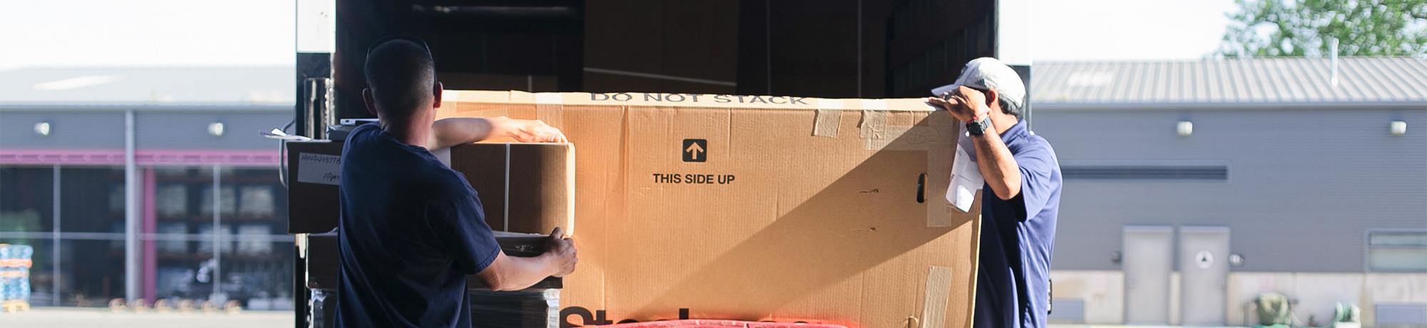 two employees of uc davis special services unloading a large box from the back at a truck